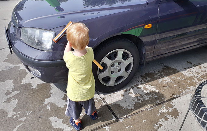 Kind säubert Auto mit Windschutzscheibenabzieher